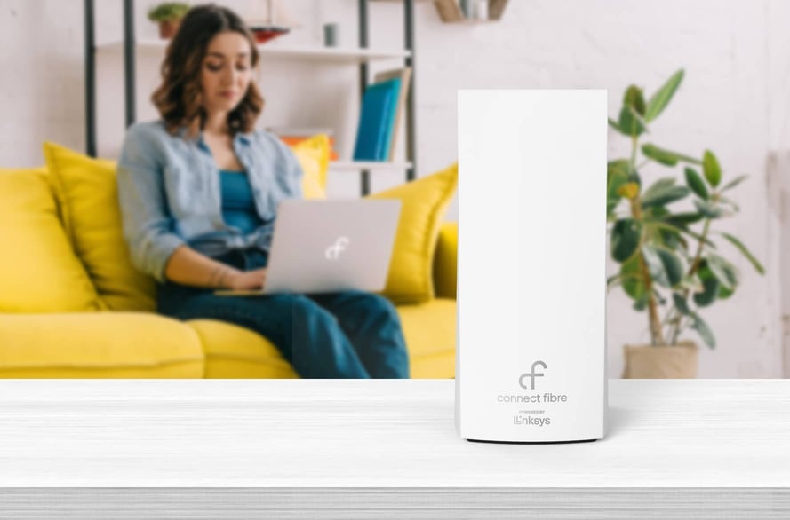 Woman using laptop on sofa with Wi-Fi 6 router in the foreground