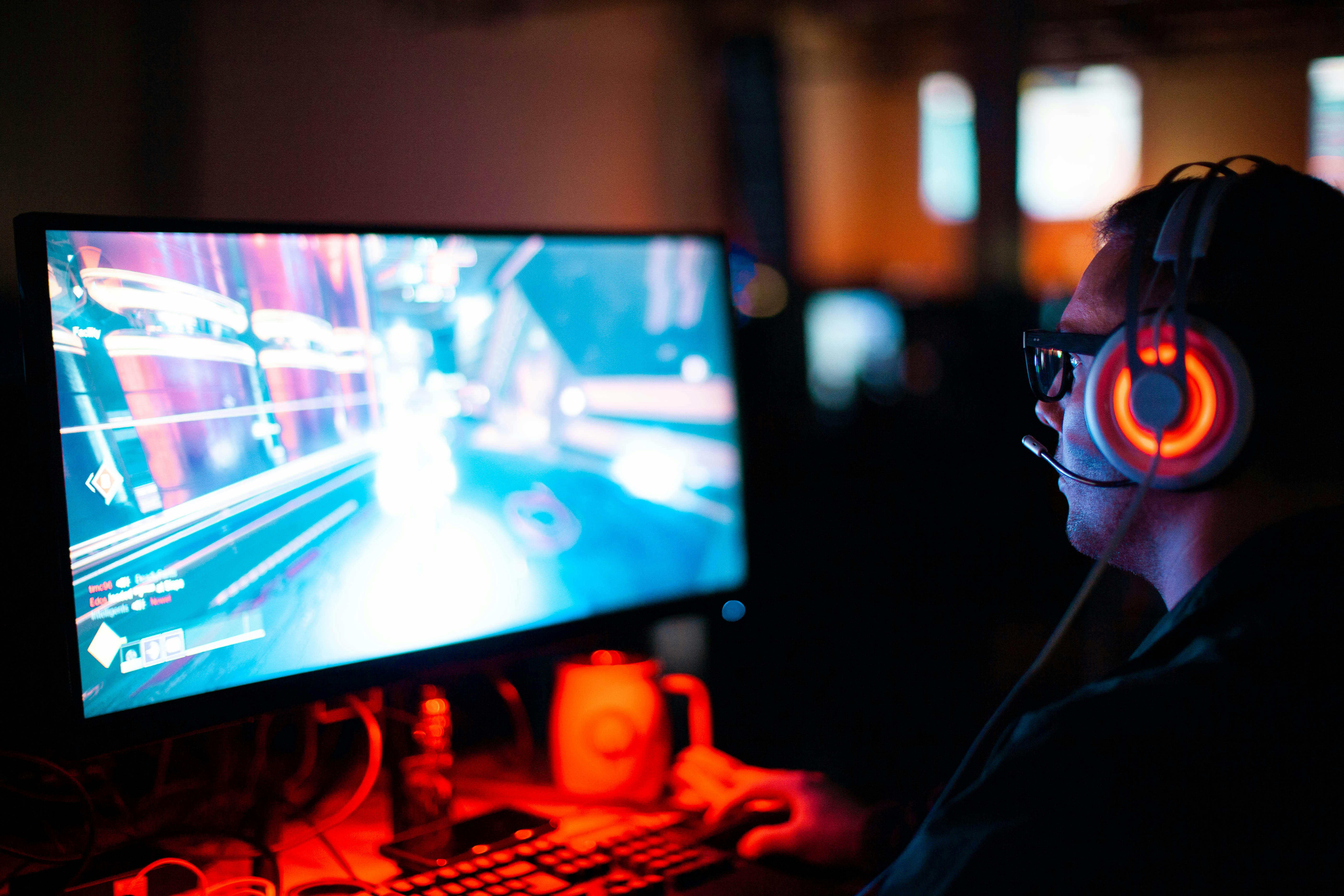 Man playing a game on a desktop in a dimly lit room while wearing a headset