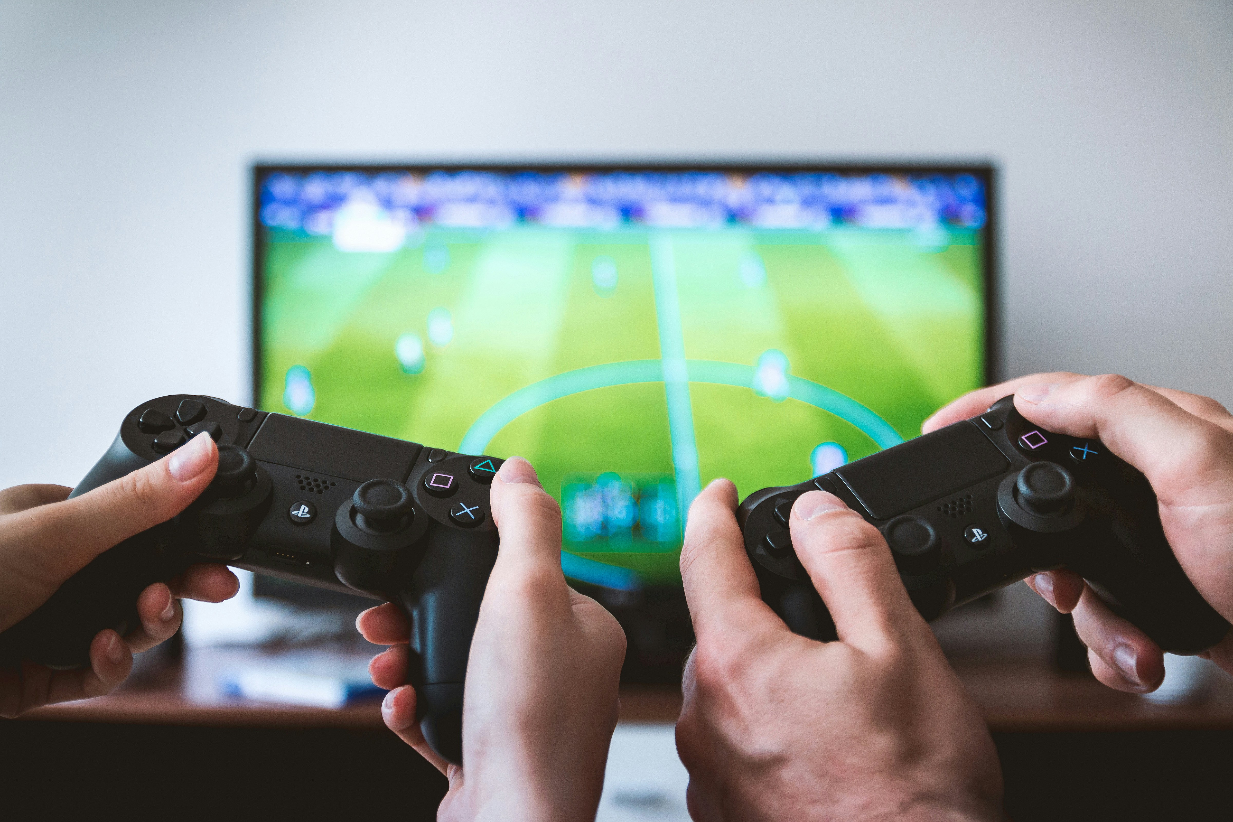 Two playstation controllers held by two hands in front of a television showing a football game